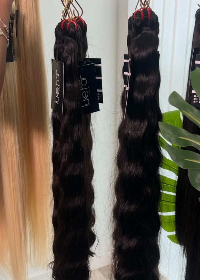 Two bundles of wavy hair extensions hanging on a rack with a plant in the background.